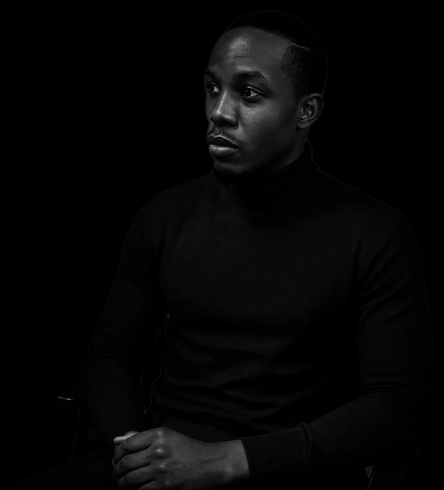 Roman Ochelo, seated, in a black turtleneck against a charcoal backdrop